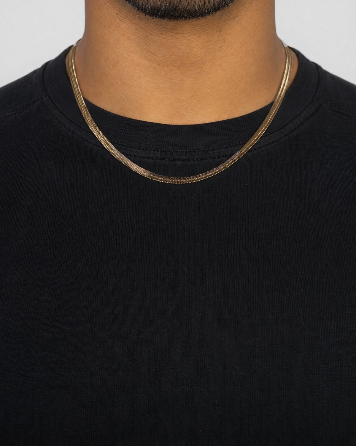Mand i sort t-shirt med herringbone-kæde i guld, set forfra