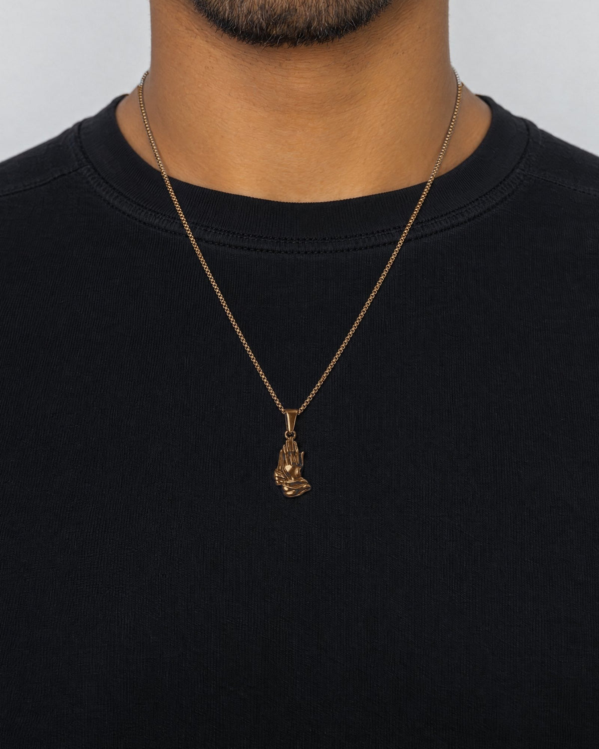 Mand i sort t-shirt med Praying Hands-vedhæng i guld, set forfra