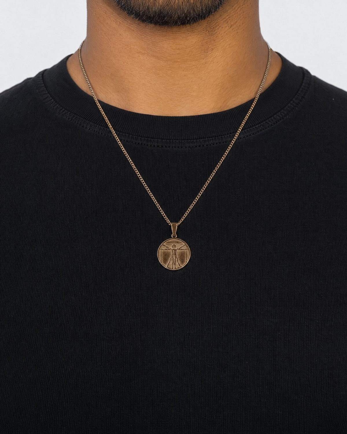 Mand i sort t-shirt med Vitruvian Man-vedhæng i guld, set forfra