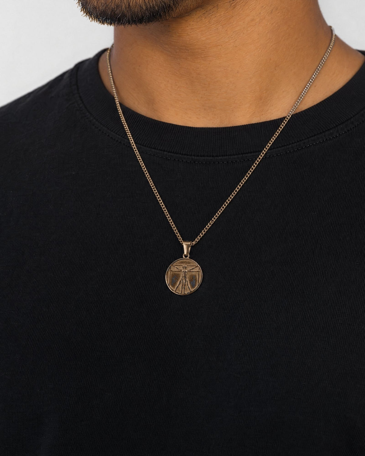 Mand i sort t-shirt med Vitruvian Man-vedhæng i guld, set fra siden